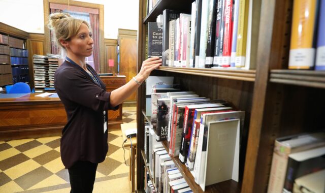 An Assembly Researcher picks out a book from a shelf in the Assembly Library.